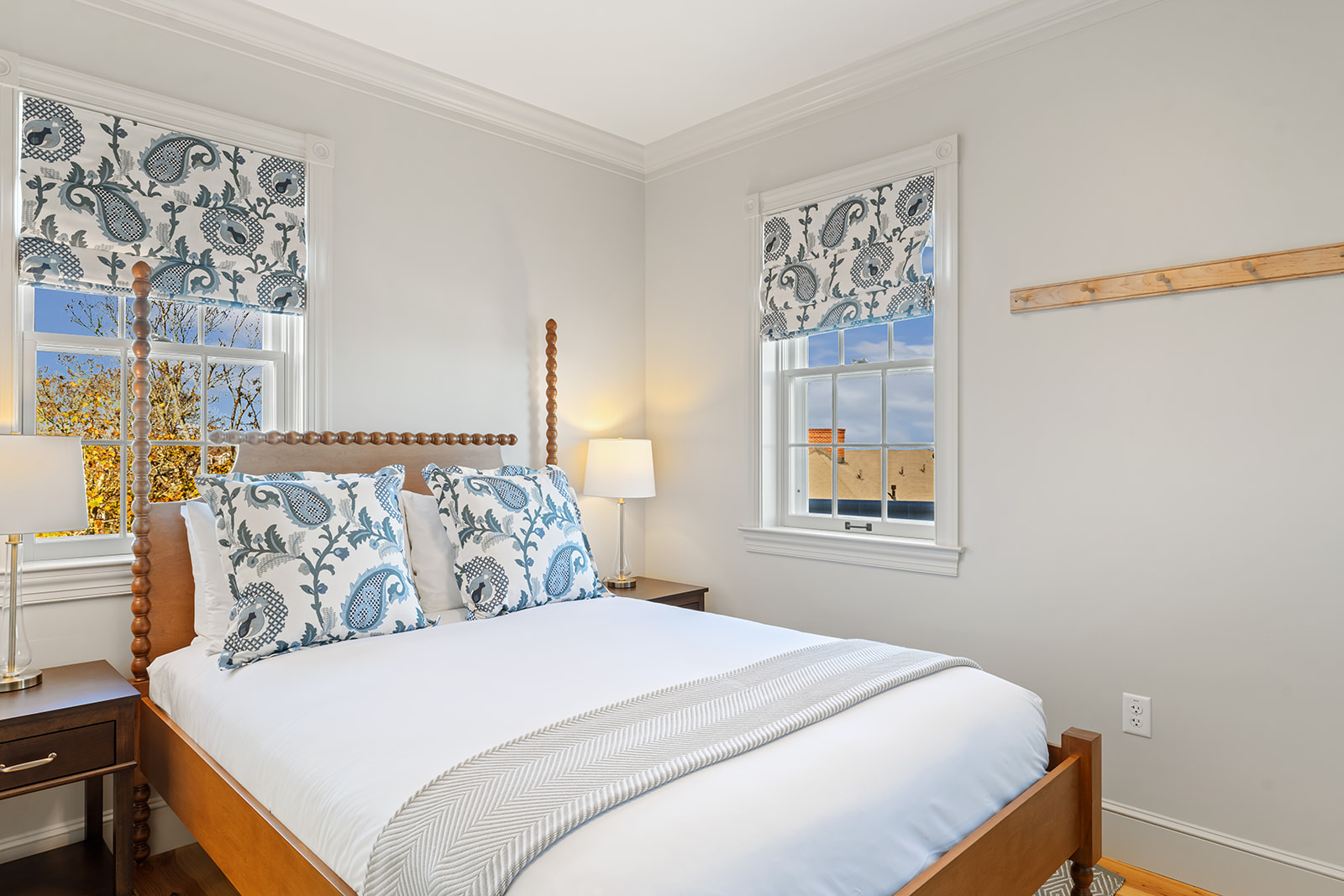 A neatly made bed with white bedding and blue accents in a room with two windows.