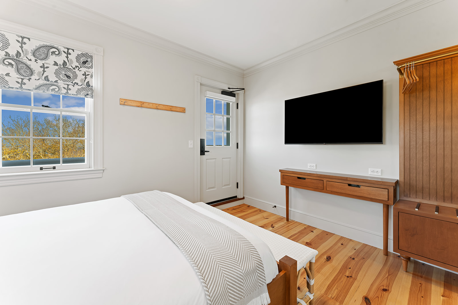 A wide view of a guest room with a bed, window, TV, desk, and closet.