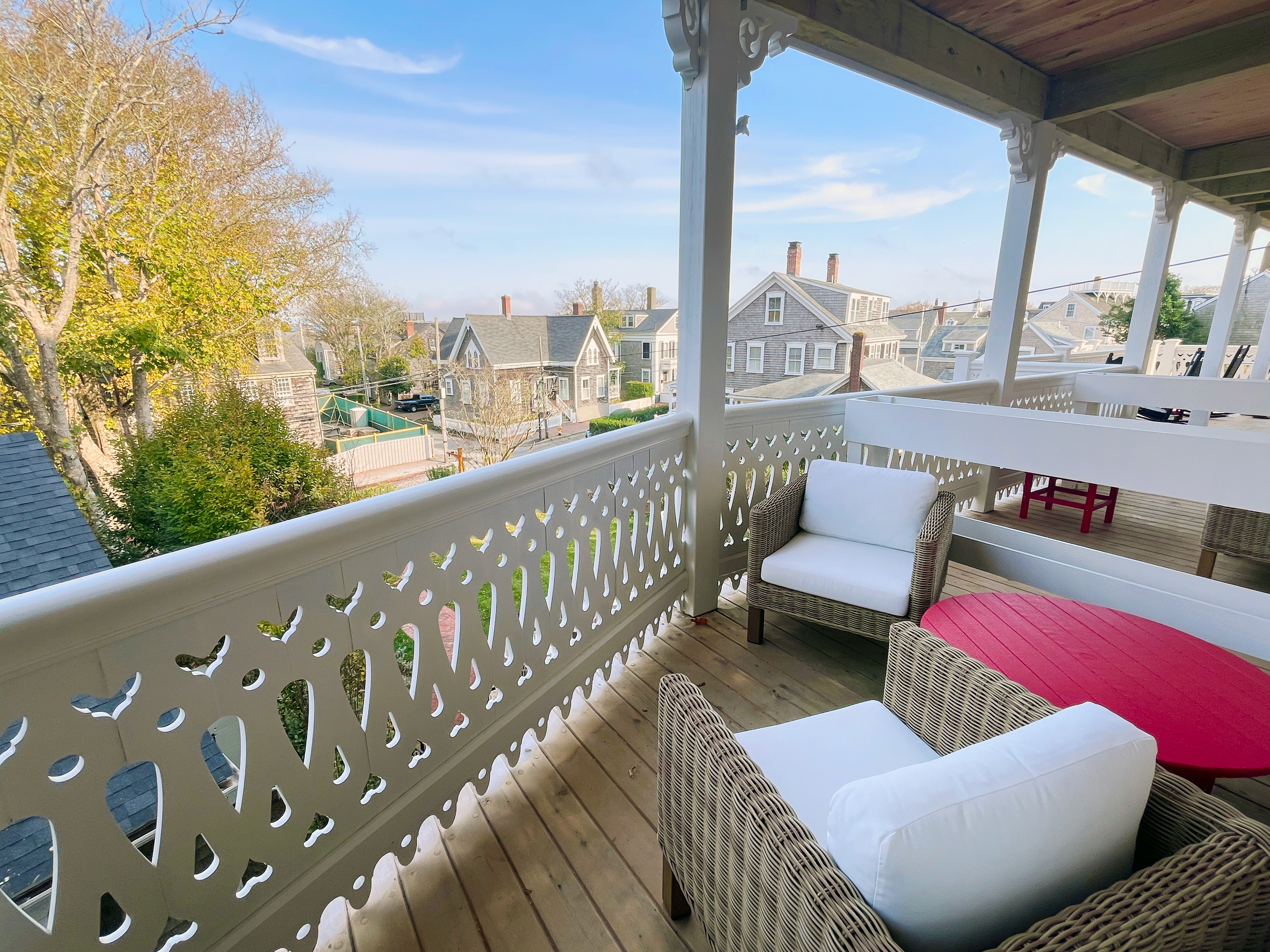 A porch with wicker furniture and a white railing overlooking a neighborhood.