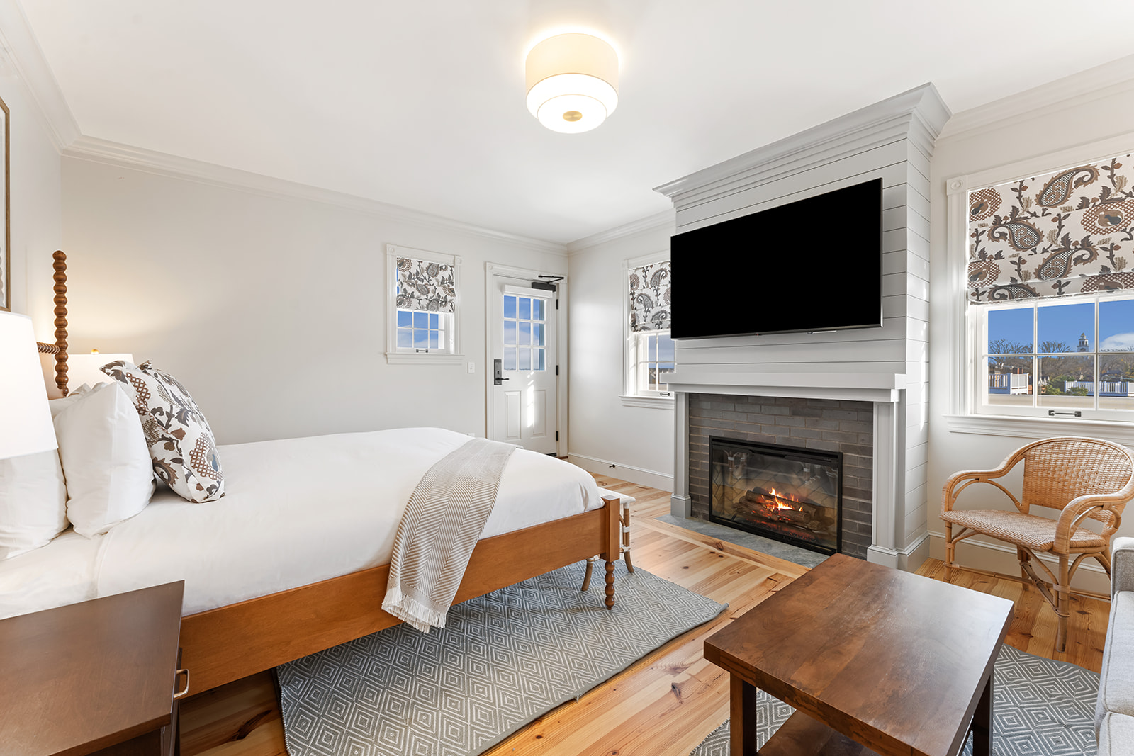 A wide view of a cozy guest room with a bed, fireplace, TV, and sitting area.