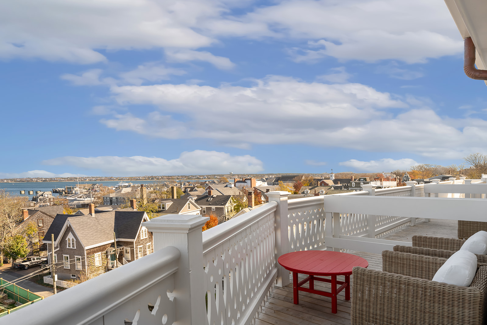 A balcony with white railing and wicker furniture overlooking a town and water.